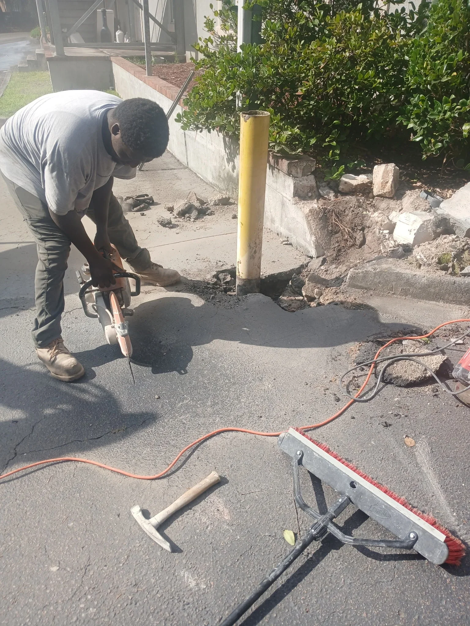 Worker using pneumatic breaker to demolish concrete driveway with debris removal and site preparation