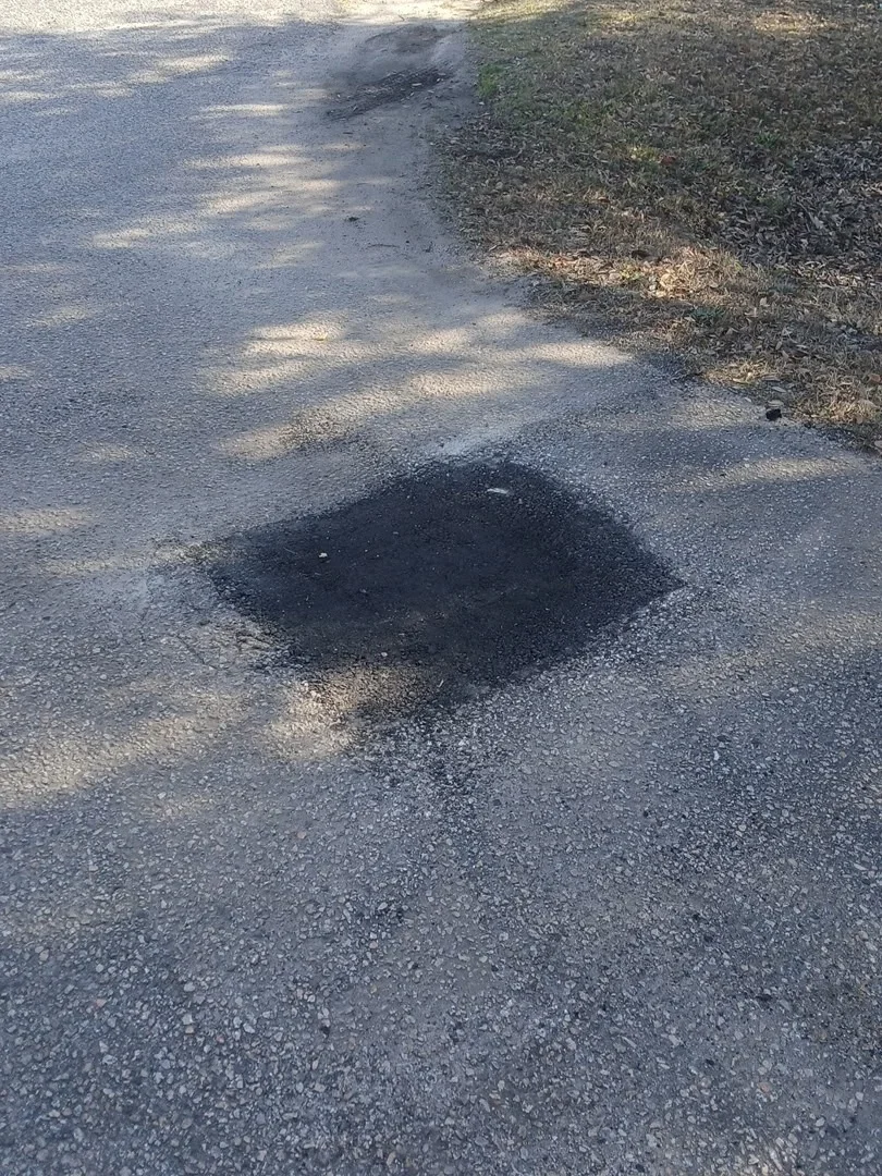 Asphalt pothole repair with fresh patch material on driveway surface
