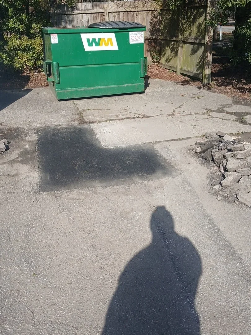 Broken concrete pad removal with exposed soil and debris pile on residential driveway