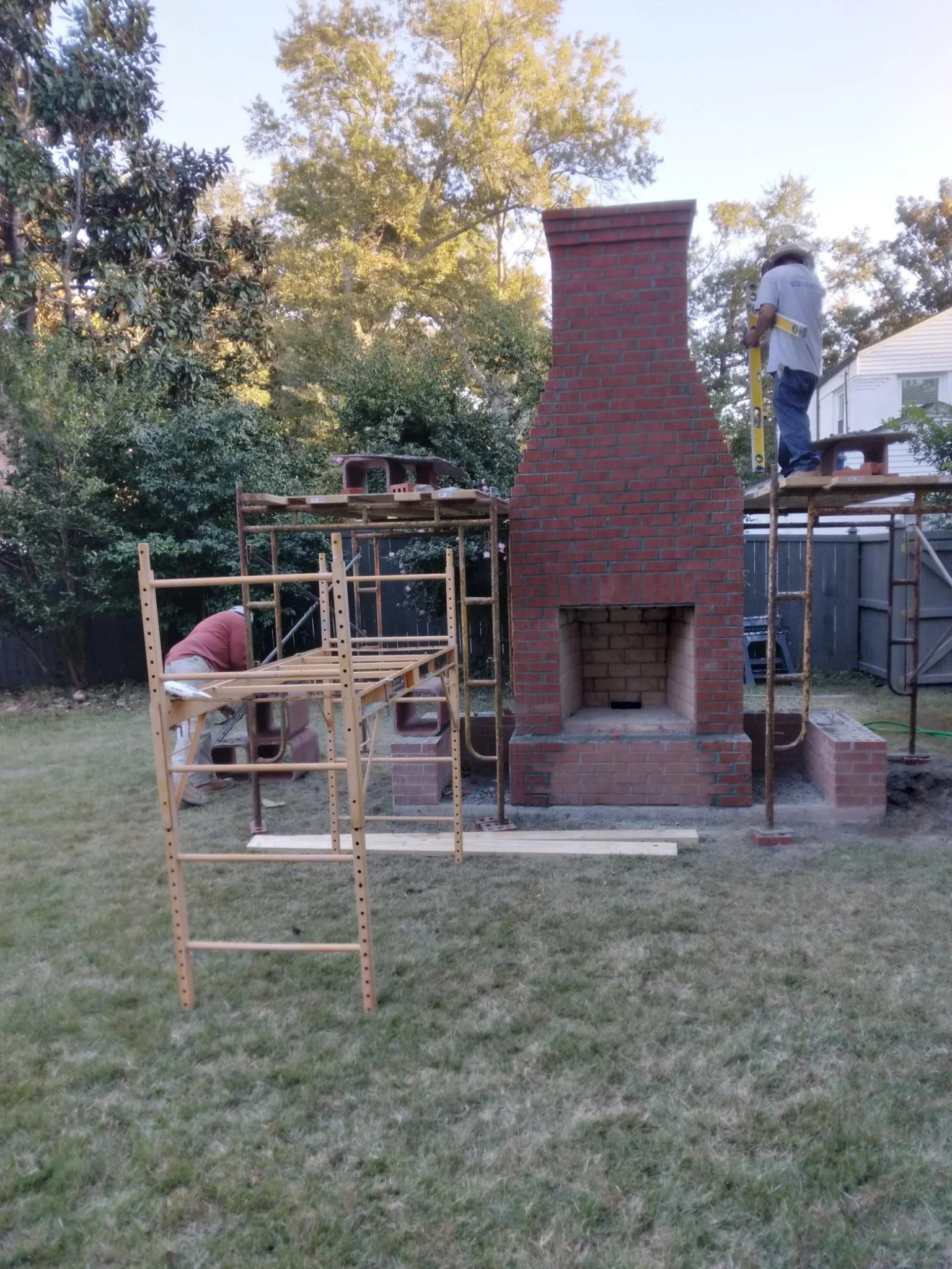 Red brick fireplace with concrete foundation and pad during construction with scaffolding