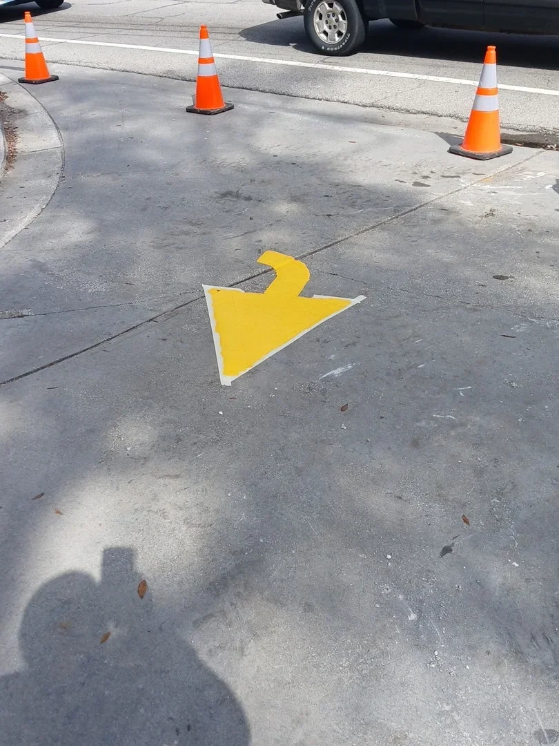 Yellow directional arrow painted on concrete parking surface with traffic cones