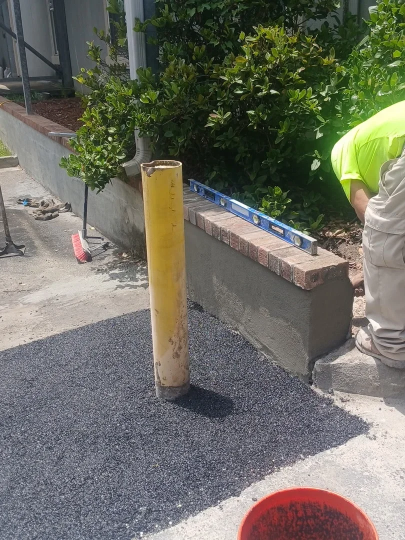 Newly installed dark aggregate concrete driveway with concrete curb and brick retaining wall edging