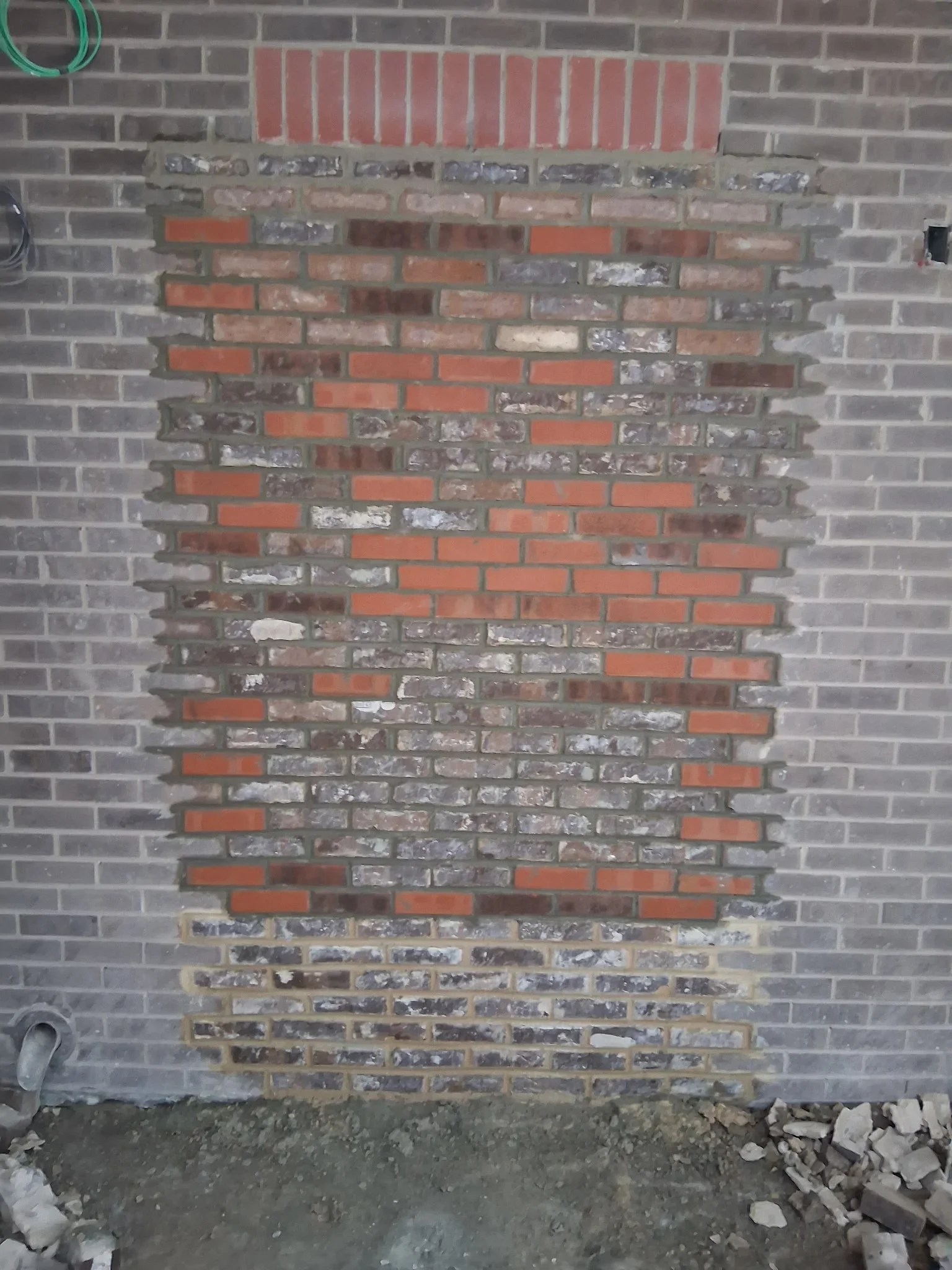 Brick veneer removal exposing concrete block wall with mixed clay brick debris