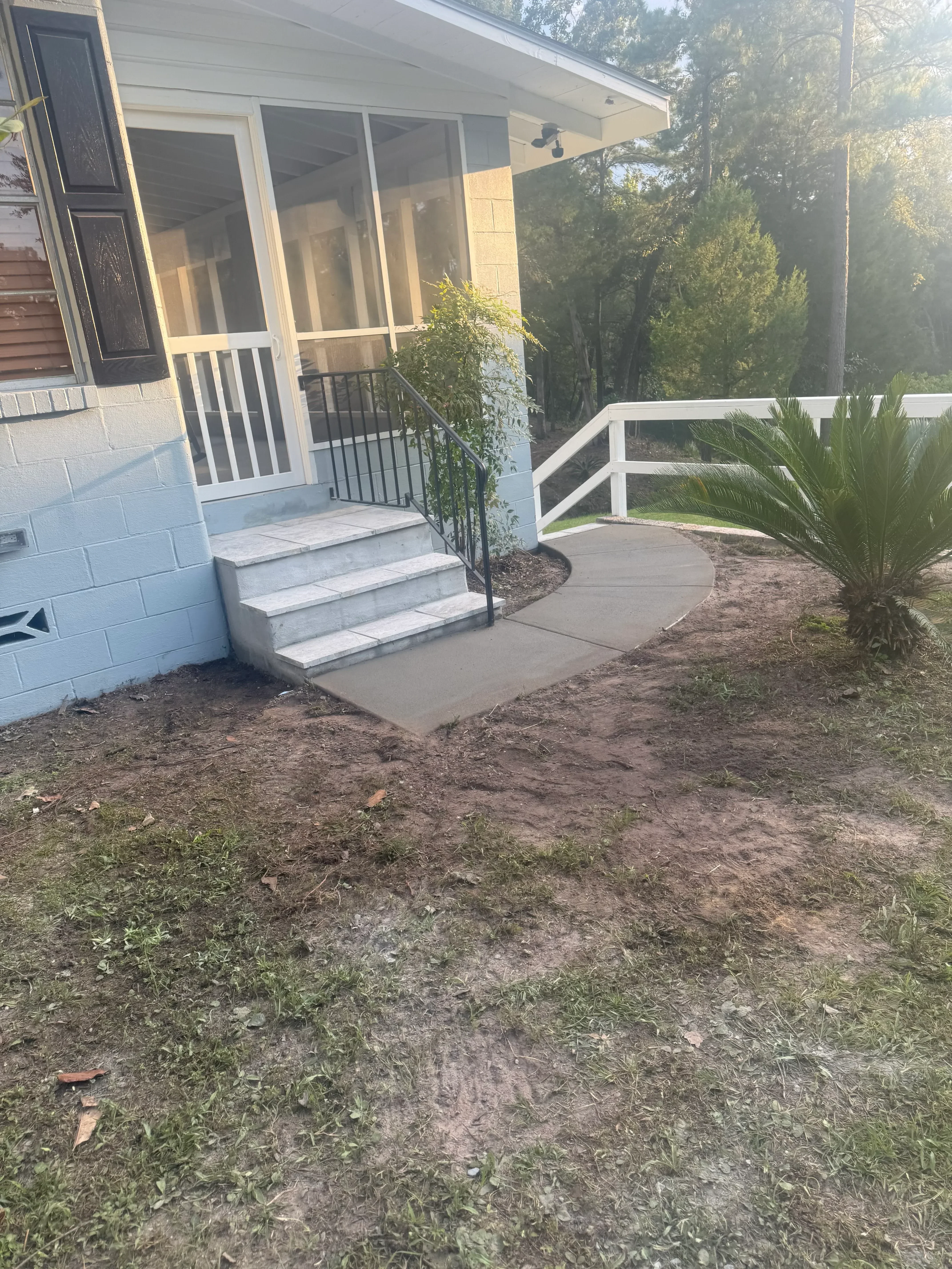 Light gray concrete patio and walkway with metal railing and integrated landscape design