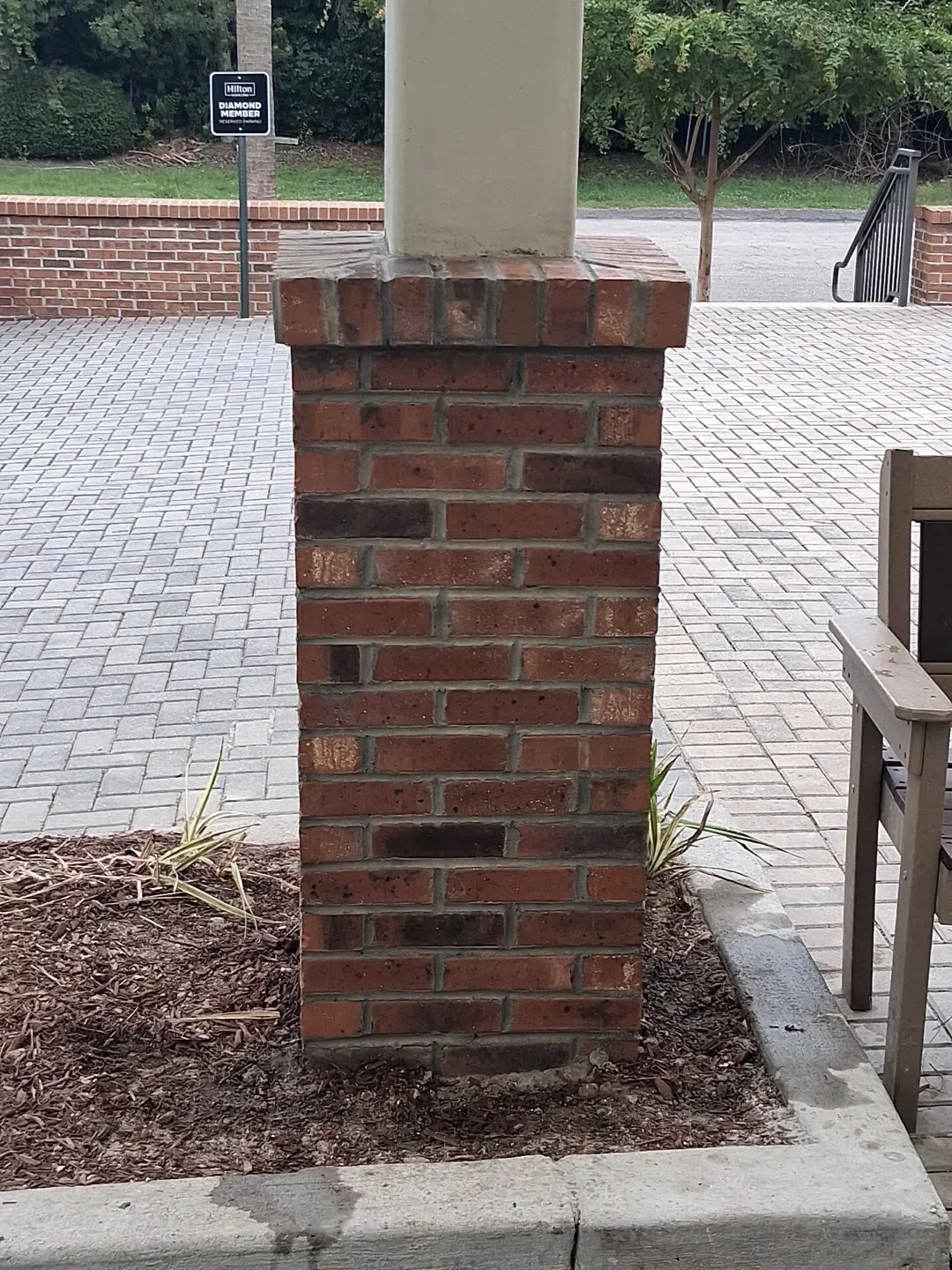 Brick column base with concrete pad and mulch bed in paved courtyard area
