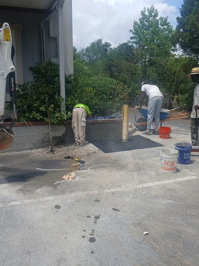 Concrete driveway installation with crew finishing fresh concrete surface and asphalt work