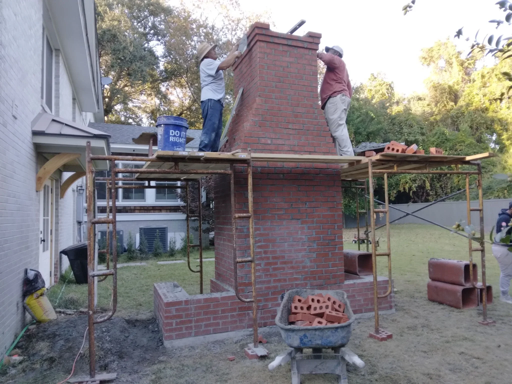 Red brick chimney under construction with metal scaffolding and concrete foundation base