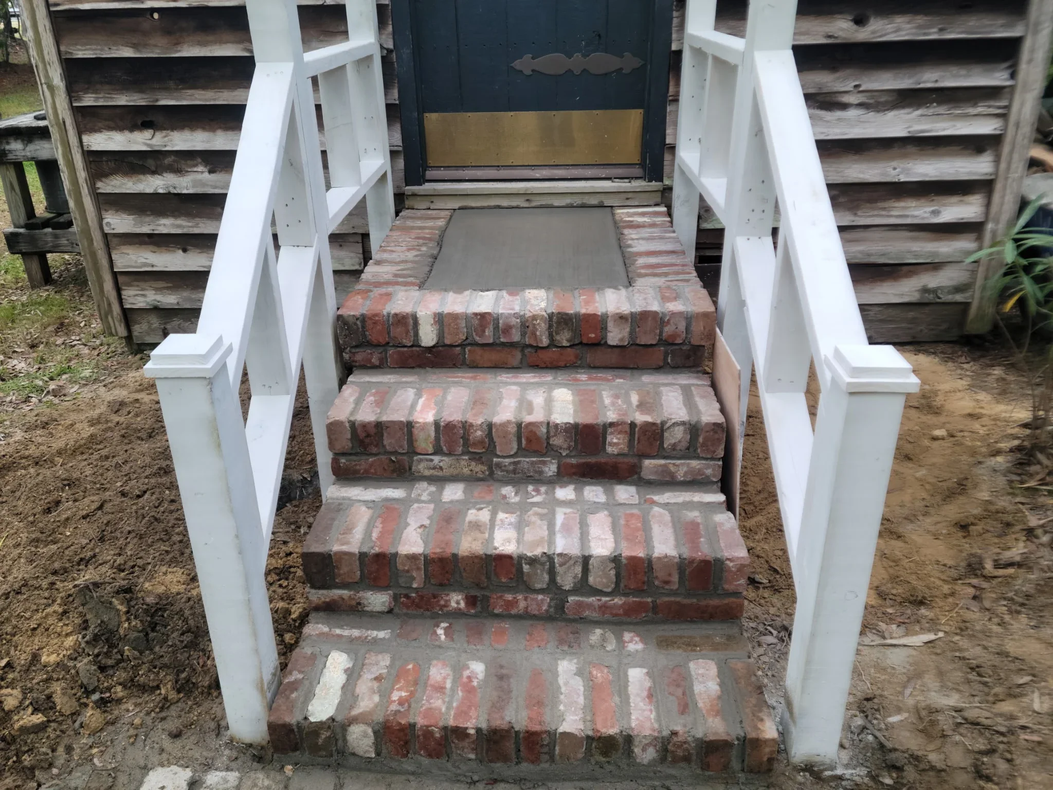 Gray concrete landing at brick stair entry with white PVC railings on both sides