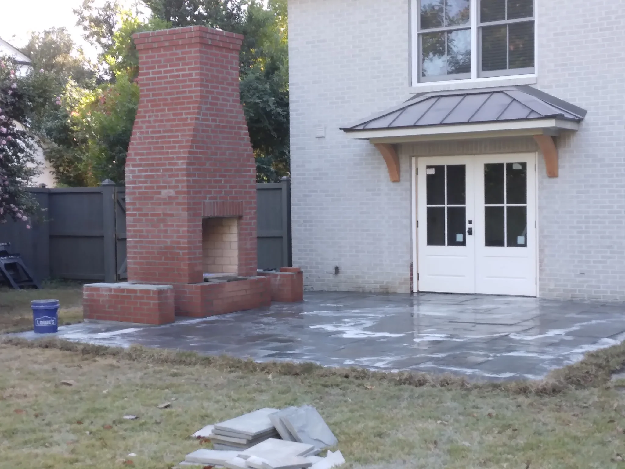Slate paver patio with mixed-size pattern installed next to brick chimney and white house