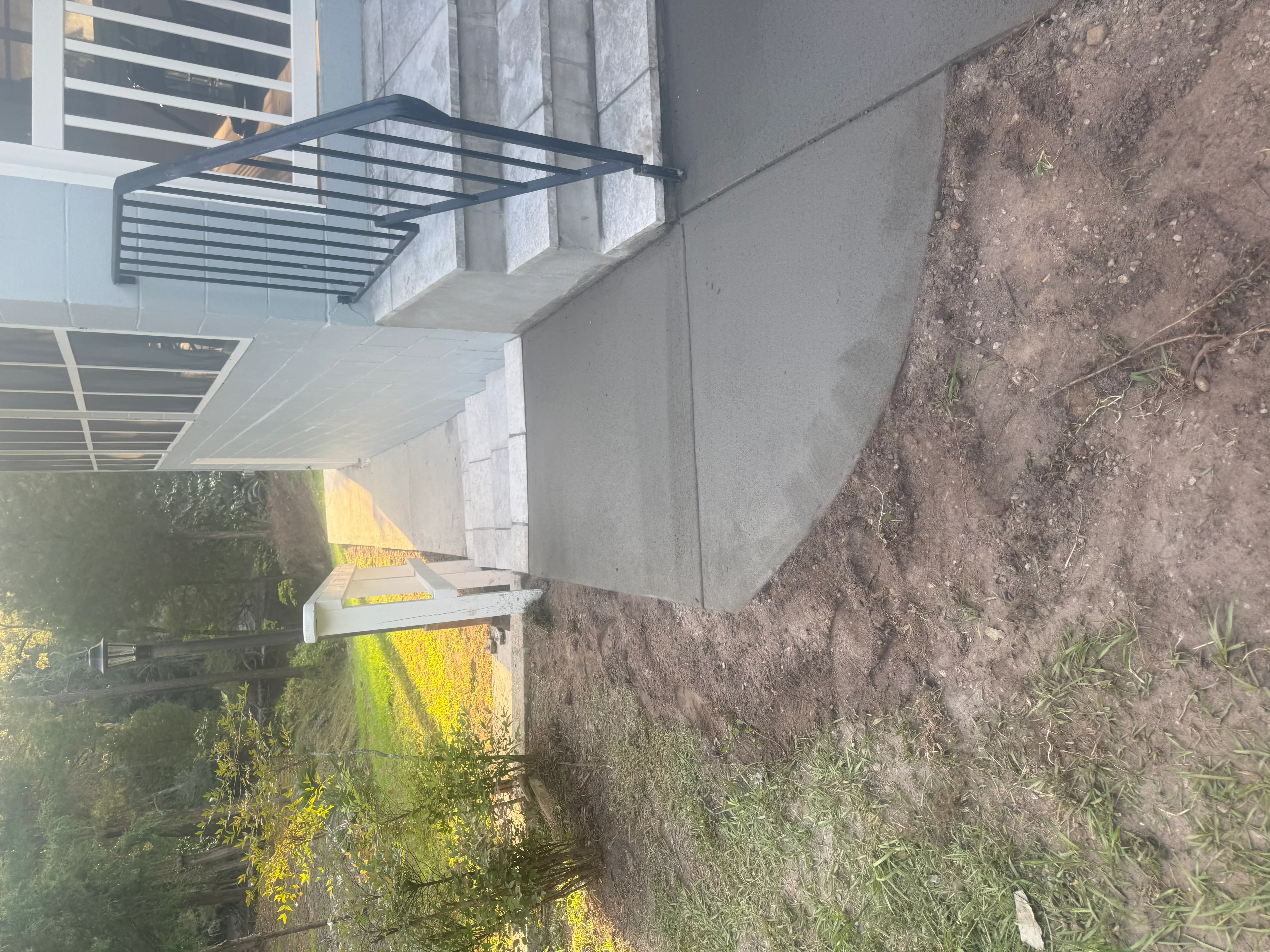 Concrete pad with metal railing next to retaining wall and graded earth