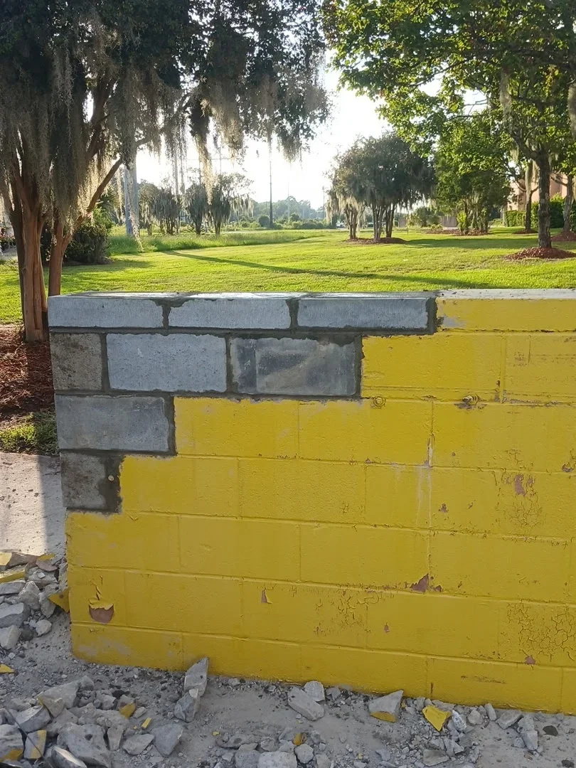 Concrete block retaining wall with yellow metal cap and coping in park setting