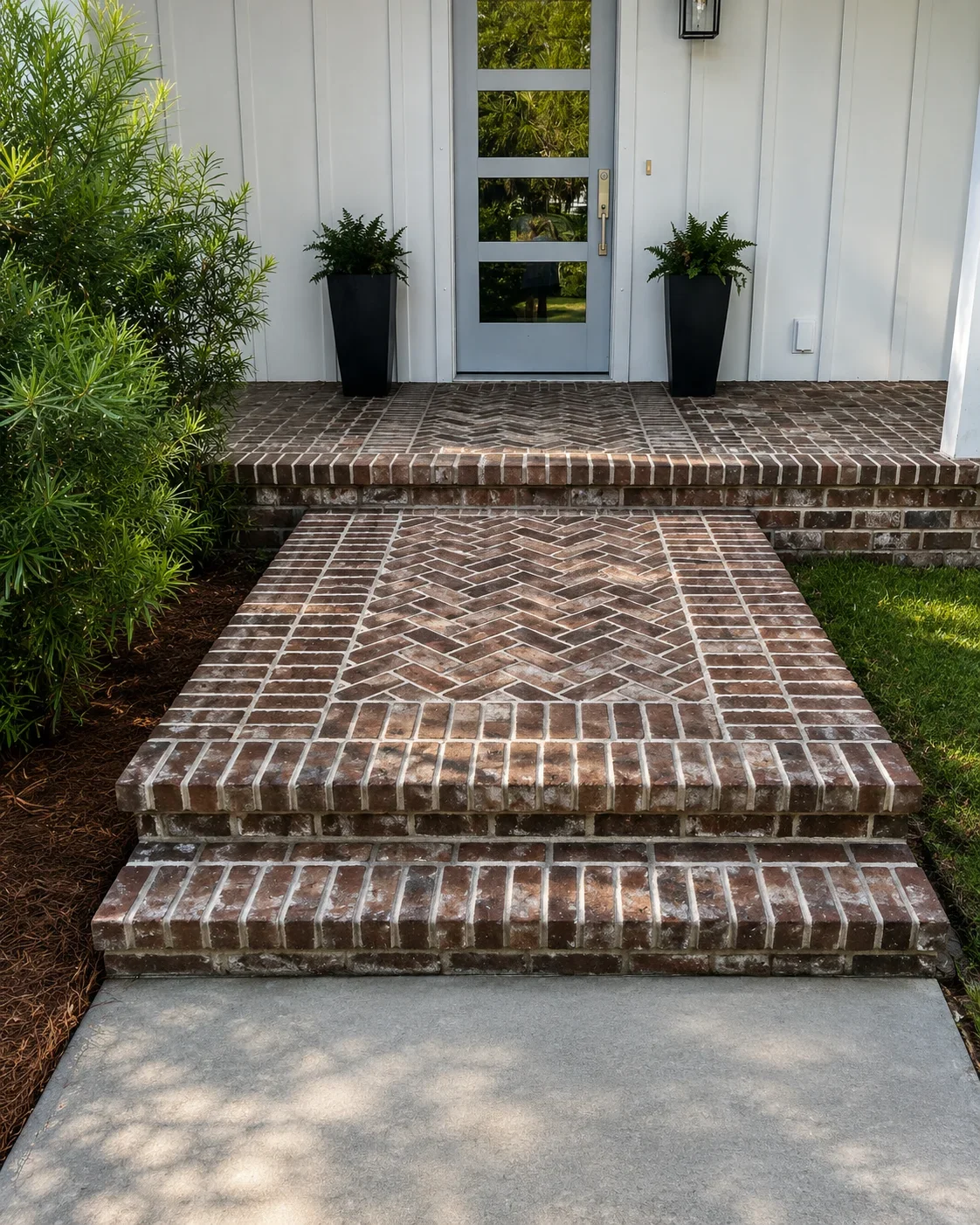 Herringbone brick concrete walkway with decorative border and steps leading to white home entrance